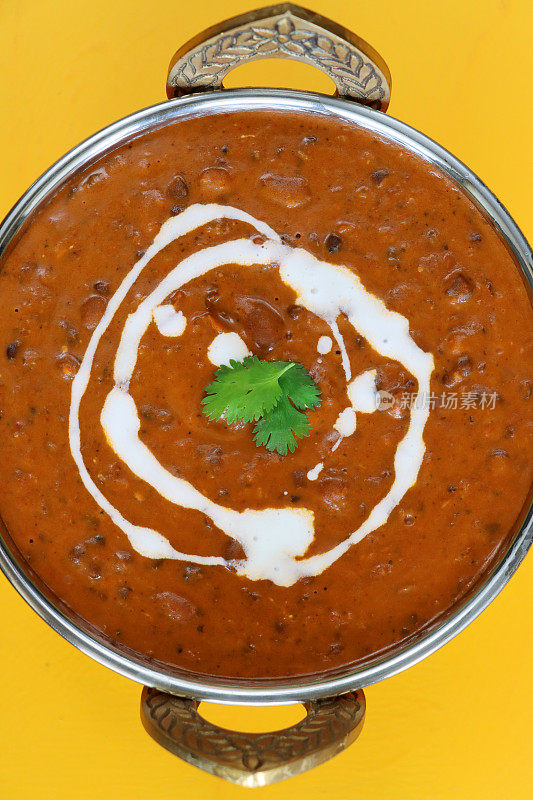 金属卡迪碗的特写图像，里面有自制的Dal makhani(黑扁豆和红腰豆咖喱)餐，黄色背景，高架视野